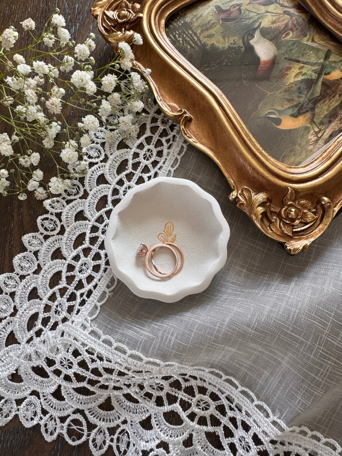 scalloped edge white clay ring dish with gold flower in center in flat lay photo