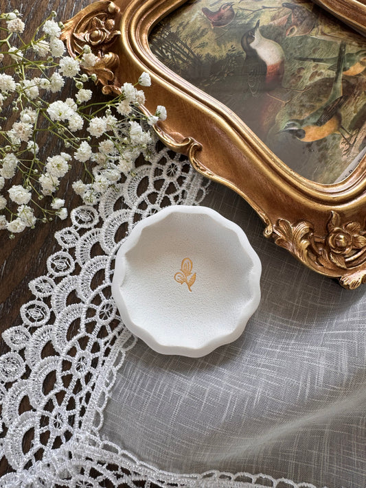 scalloped edge white clay ring dish with gold flower in center in flat lay photo